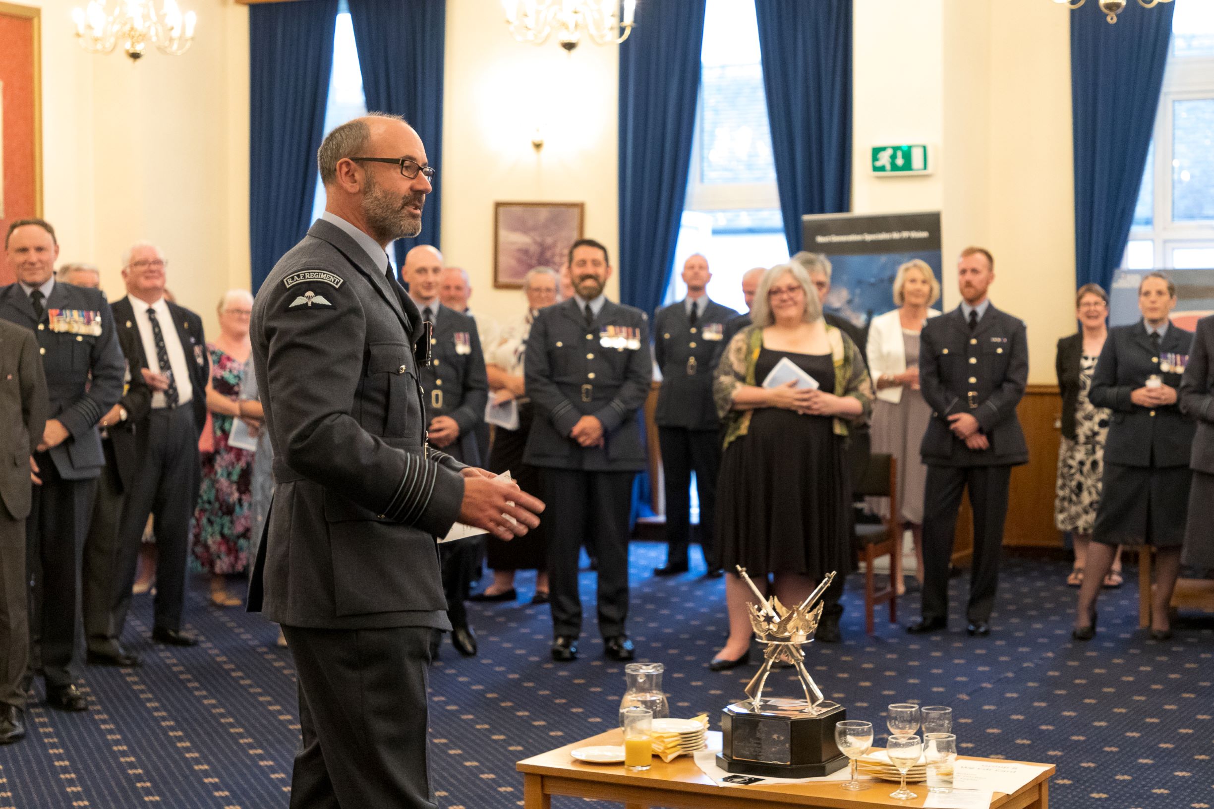 Image shows aviators and guests gathered as aviator gives speech to room.